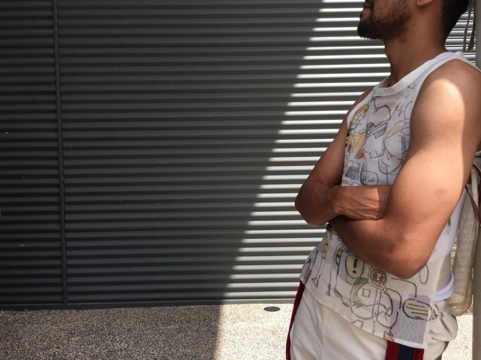 Person leaning on wall with arms crossed, wearing a nice arty singlet.